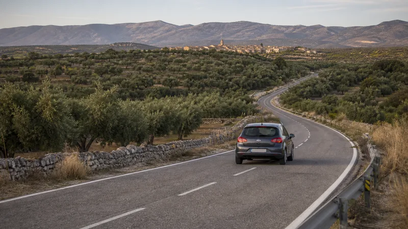 Coche en una carretera entre olivares y un núcleo rural del interior