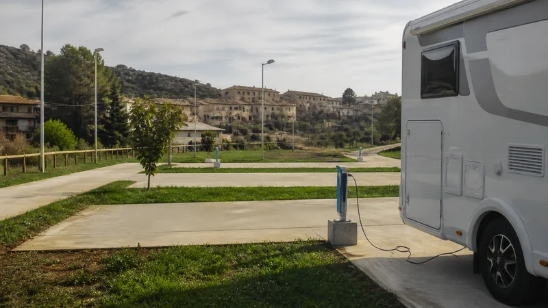 Composición editorial genérica y exclusiva de área autorizada de autocaravanas limpia junto a un pueblo; no representa horarios, aforo ni condiciones en tiempo real