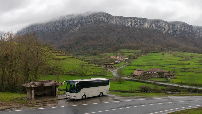 Autobús regional en un valle verde con pueblos de piedra y pared caliza