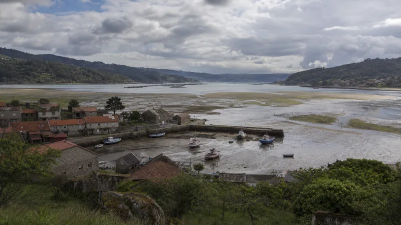 Ría en bajamar con puerto pesquero, marismas, casas de piedra y bateas
