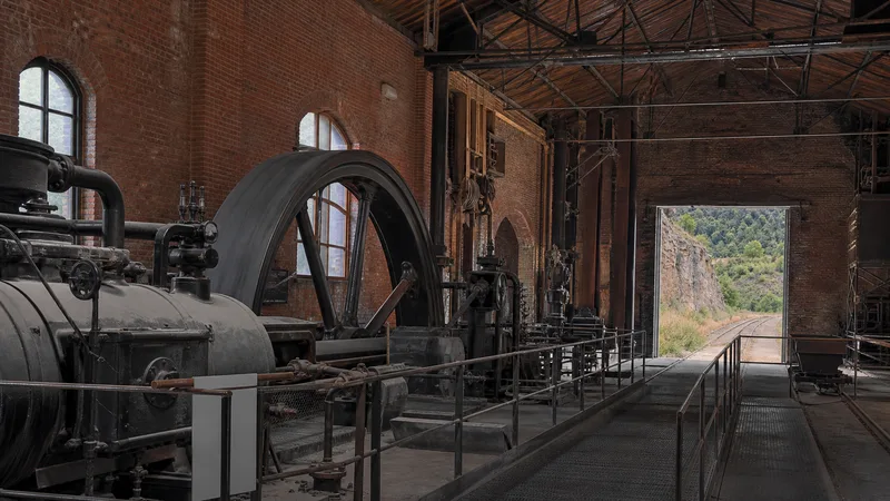 Nave de ladrillo con máquina histórica, pasarela y vía hacia el paisaje