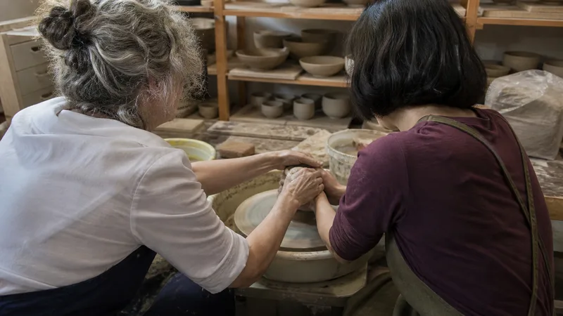 Maestra alfarera guía las manos de una aprendiz ante un torno