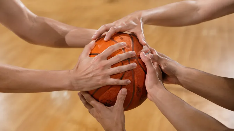 Manos de varias jugadoras disputan un balón de baloncesto sin marcas sobre una pista cubierta