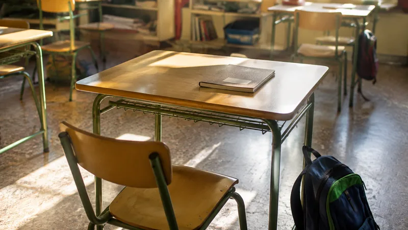 Mesa escolar vacía con un cuaderno y una mochila en un aula