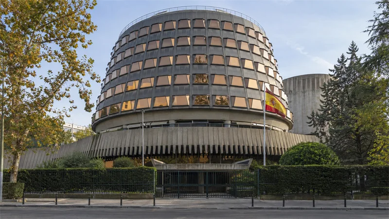 Fachada curva del Tribunal Constitucional en Madrid, con la bandera de España junto a la entrada.